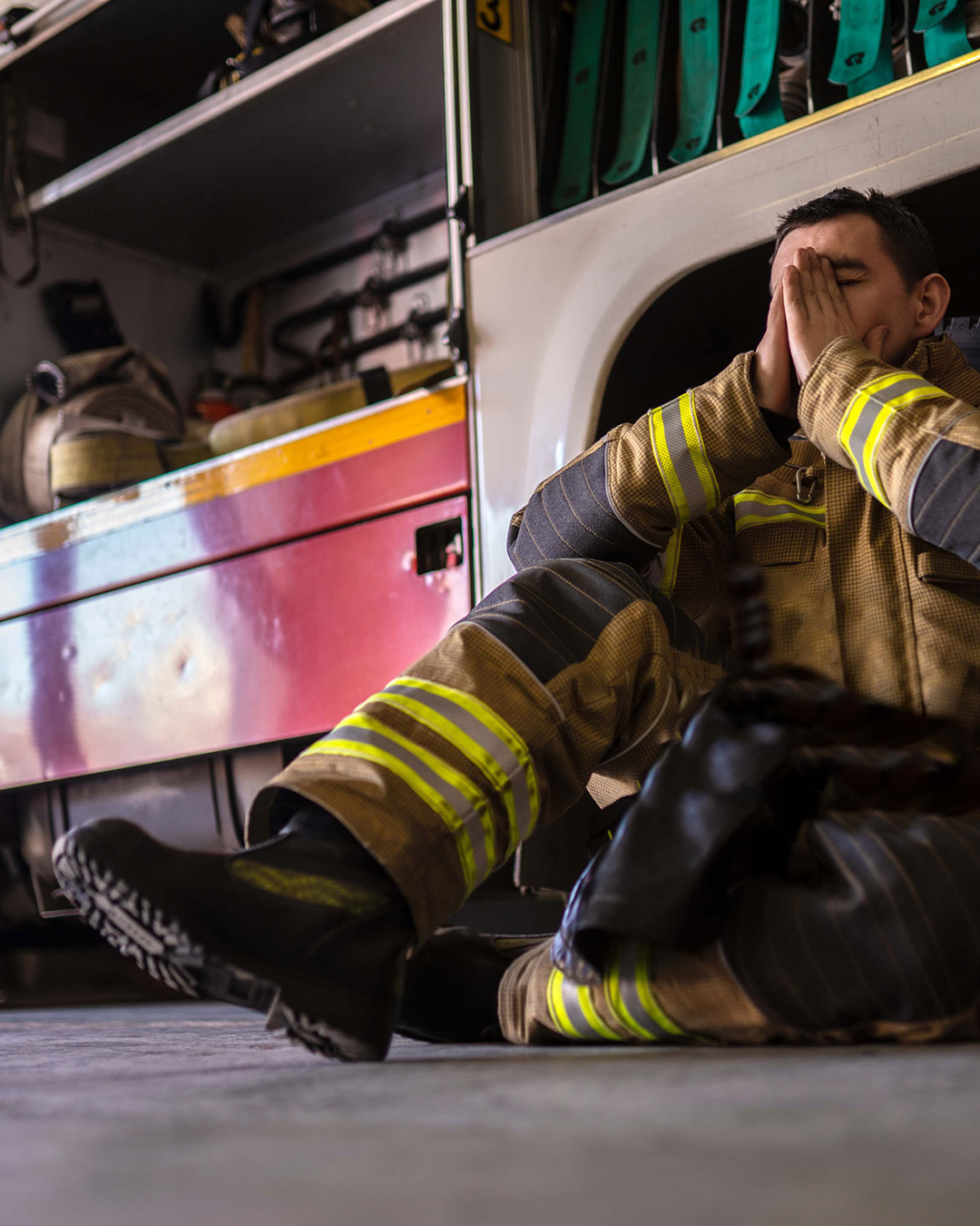Firefighter sitting in front of firetruck covering face with hands